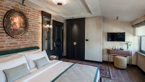 Una habitación de hotel con una cama grande, una pared de ladrillo, una puerta oscura, un televisor y una pequeña mesa con un florero.