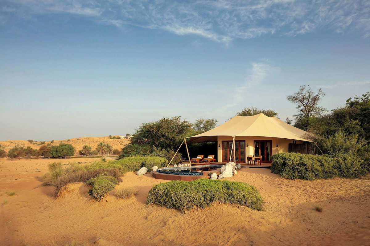 Una tenda al desert amb terrassa, envoltada de dunes de sorra i vegetació escassa.