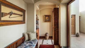 A hallway with a wooden bench, a framed rifle, a vase, and a door leading to another room.