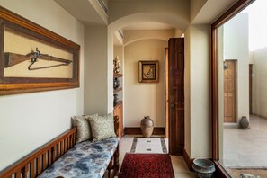 A hallway with a wooden bench, a framed rifle, a vase, and a door leading to another room.