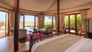 A spacious bedroom with a large bed, a sitting area with chairs, a small table, and a view of the desert landscape through large windows. - Al Maha, A Luxury Collection Desert Resort & Spa, Dubai (Murqquab)