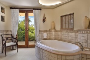 A bathroom with a large bathtub, a wooden bench, and a view of greenery outside.