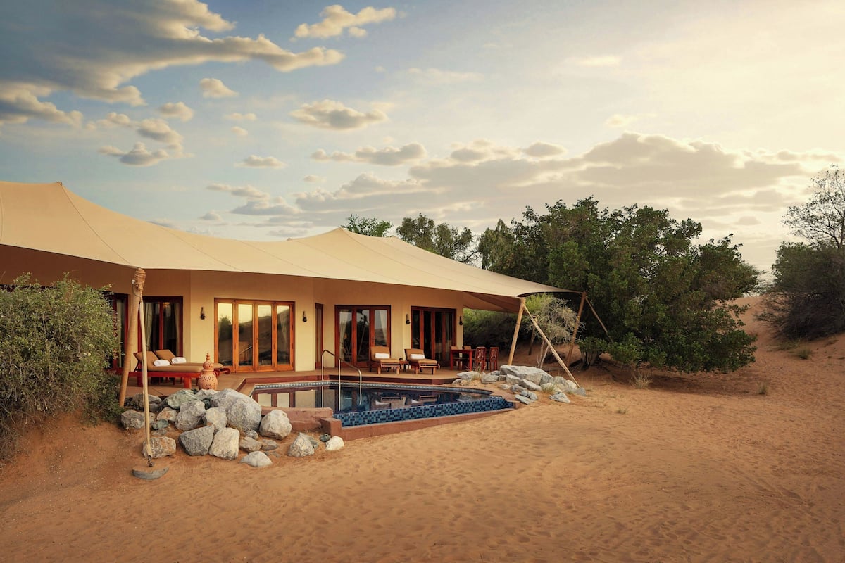 Un complex turístic al desert amb una piscina, mobiliari exterior i una àmplia tanca.