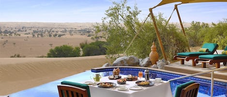 A dining area with a pool overlooking a desert landscape.