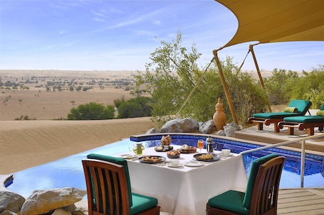 A dining area with a pool overlooking a desert landscape.