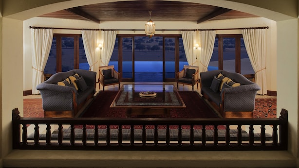 A room with a large window, two armchairs, a coffee table, and a view of the ocean at night. - Al Maha, A Luxury Collection Desert Resort & Spa, Dubai (Murqquab)
