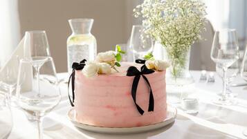 A round cake with white flowers and black ribbons on a white tablecloth.