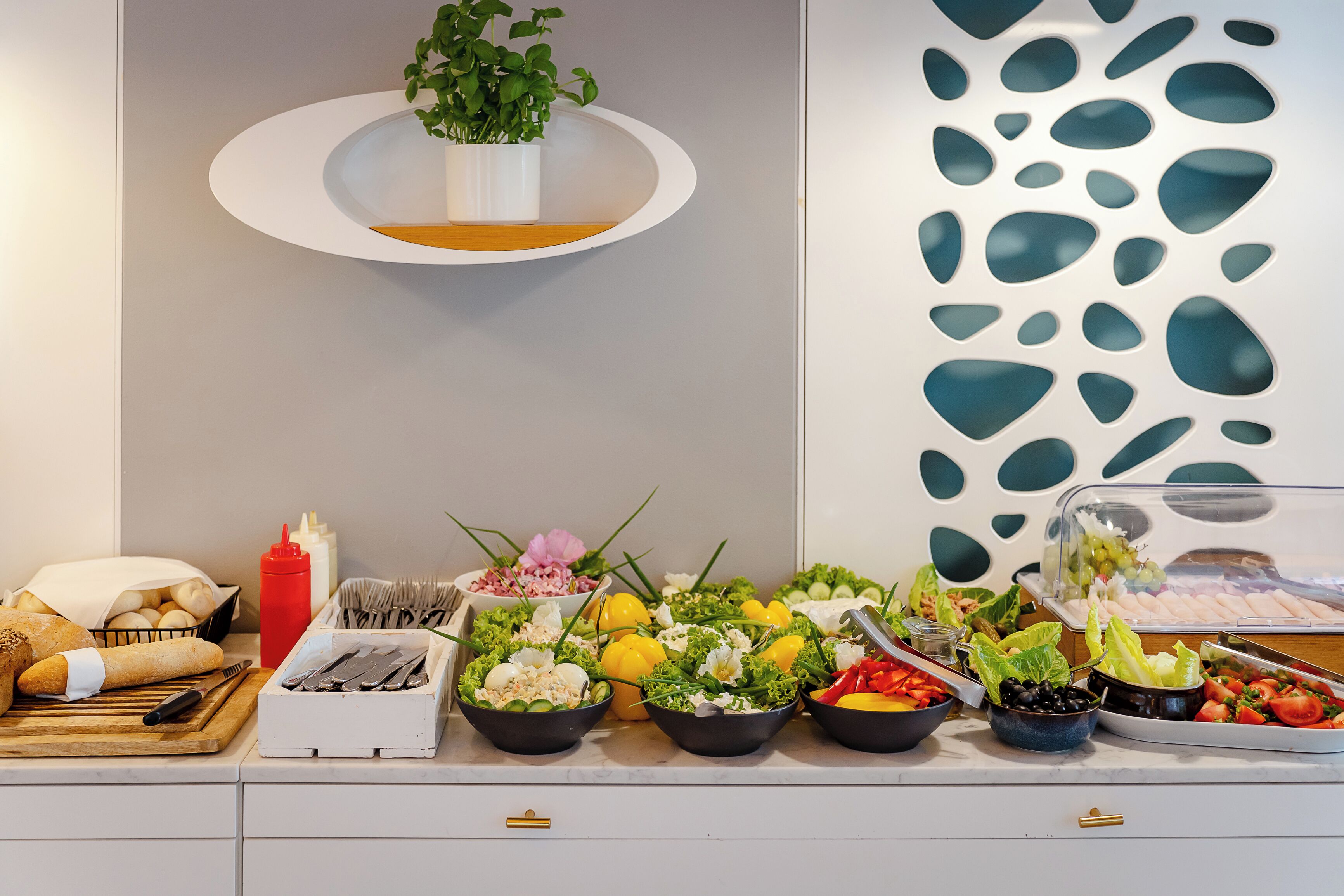 A buffet setup with various food items, utensils, and a decorative plant.
