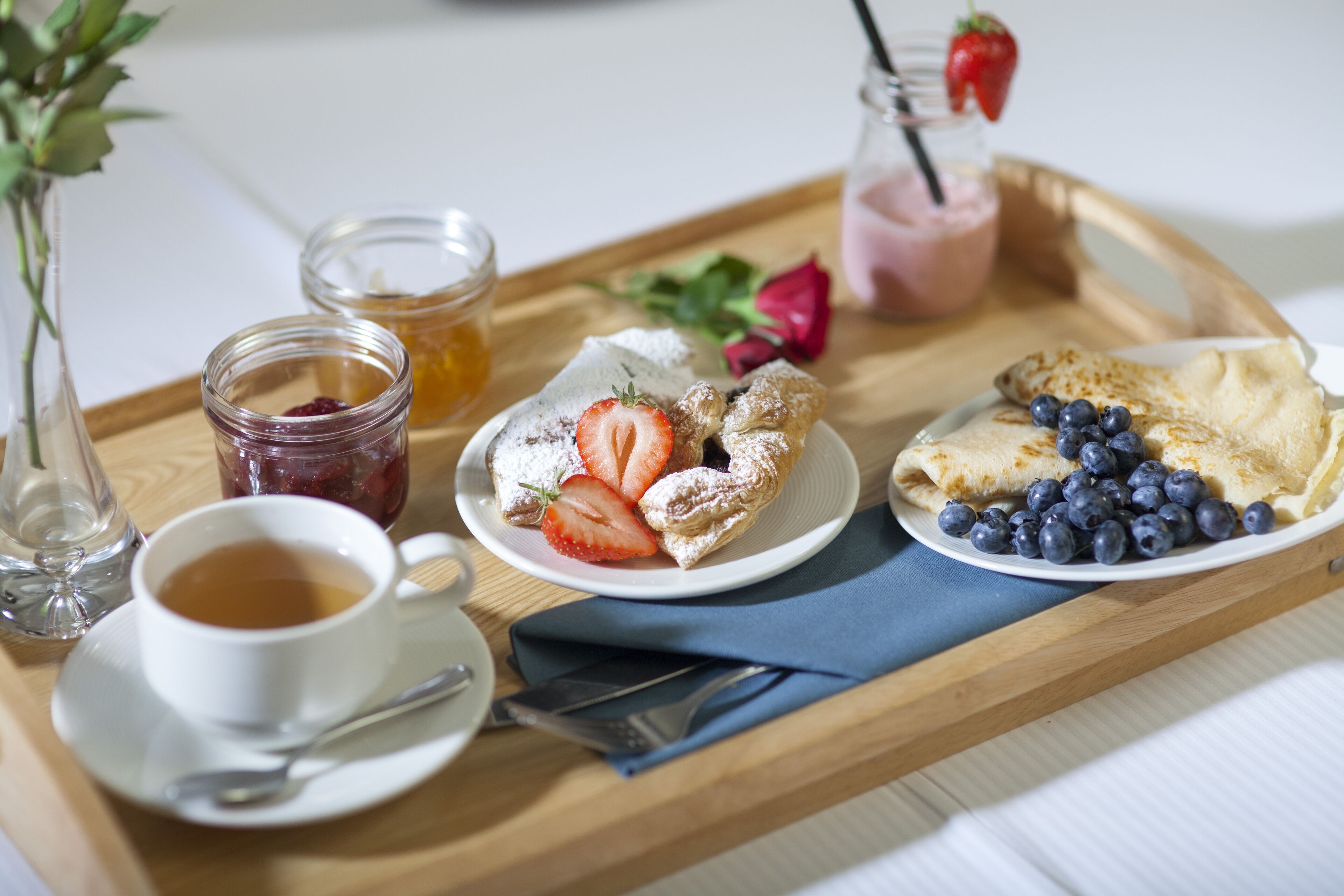 A tray with a cup of tea, a plate of pastries, and a glass of strawberry smoothie.