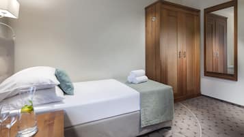 A hotel room with a bed, a wooden wardrobe, a bedside table with a glass and a bottle, and a mirror on the wall.
