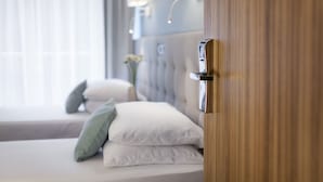 Habitación de hotel con cama, almohadas, mesita de noche y lámpara fijada a la pared.