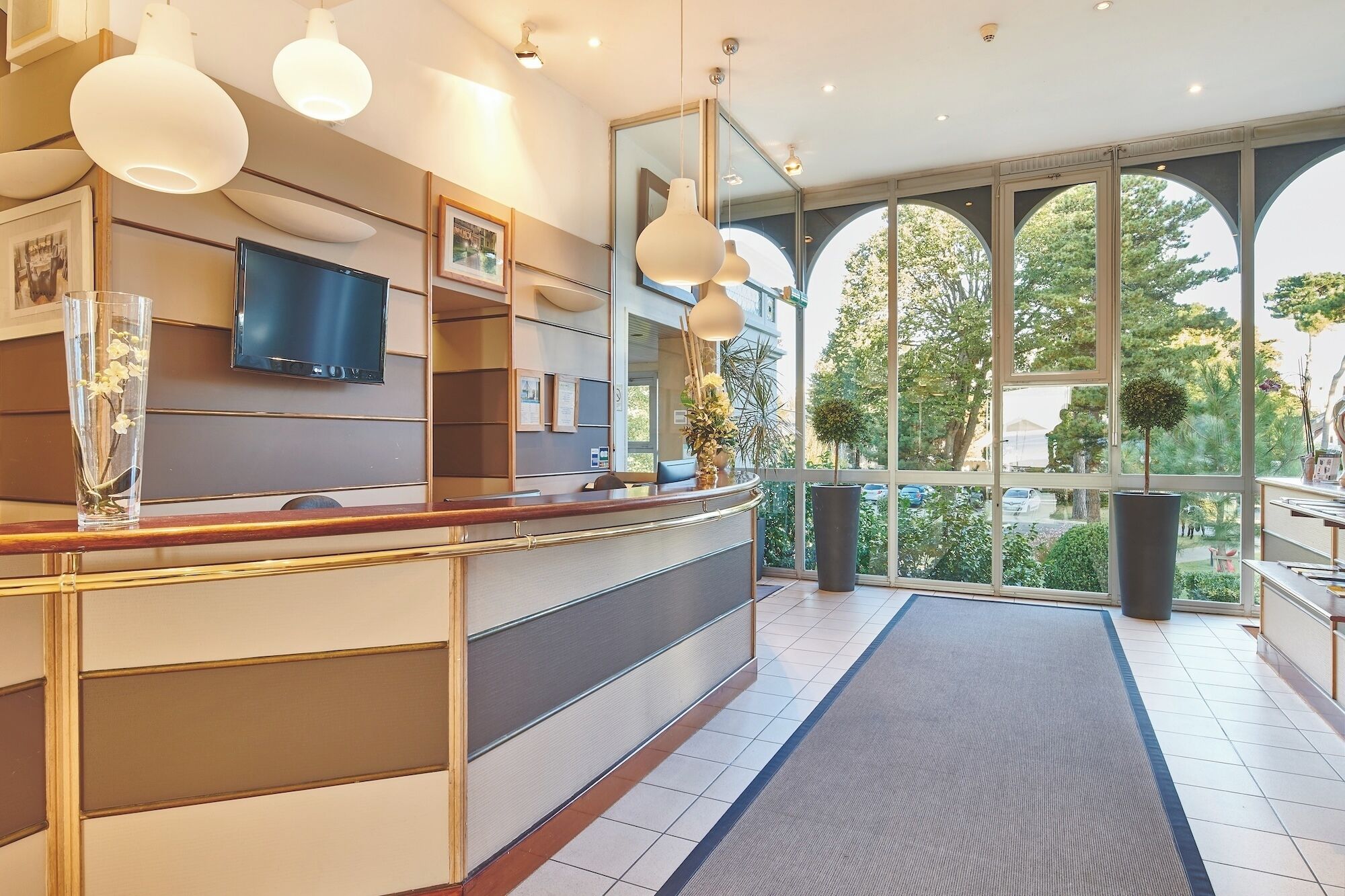 Un hall d’hôtel moderne avec un comptoir d’accueil, de grandes fenêtres et des plantes d’intérieur.