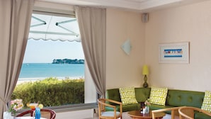 A room with a green sofa, wooden chairs, a small table with drinks, and a view of the sea. - Hôtel Vacances Bleues Villa Caroline (La Baule-Escoublac)