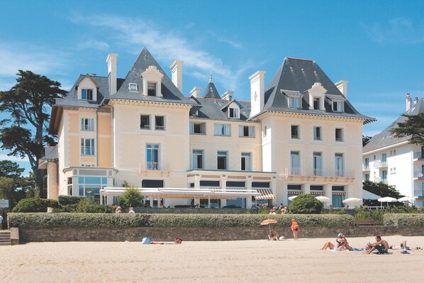 A large, multi-story building with a symmetrical facade, multiple chimneys, and a balcony with a railing.