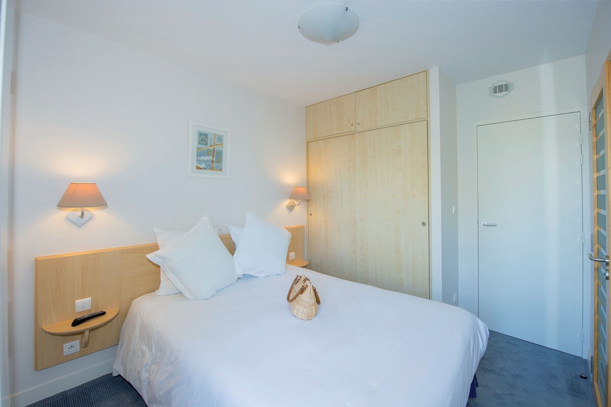 Ein Hotelzimmer mit Bett, Nachttischlampen, einem Holzkopfteil, einem Kleiderschrank und einer Tür.