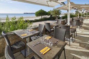 An outdoor dining area with tables and chairs, overlooking a beach.