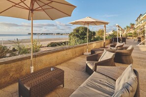 A seaside patio with wicker furniture and umbrellas, overlooking the beach.