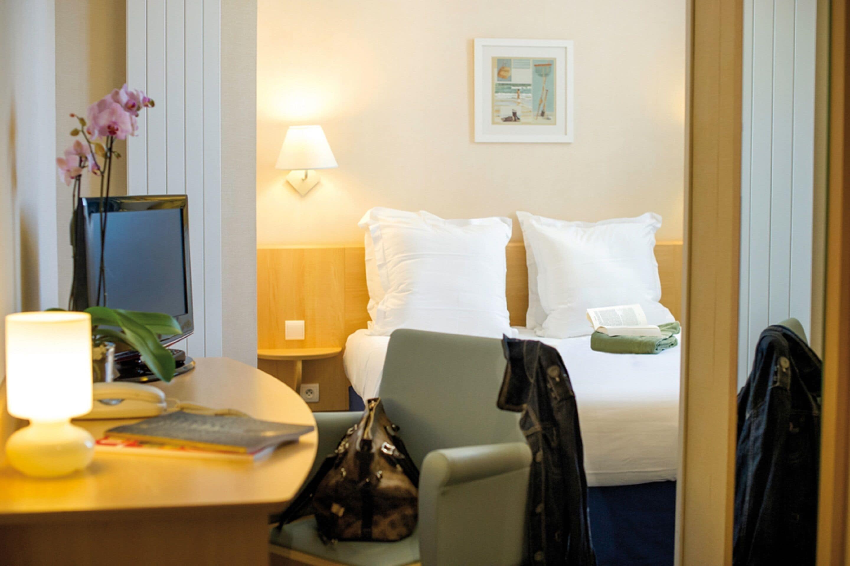 Une chambre d’hôtel avec un lit, un bureau doté d’une lampe, une chaise et une petite table.