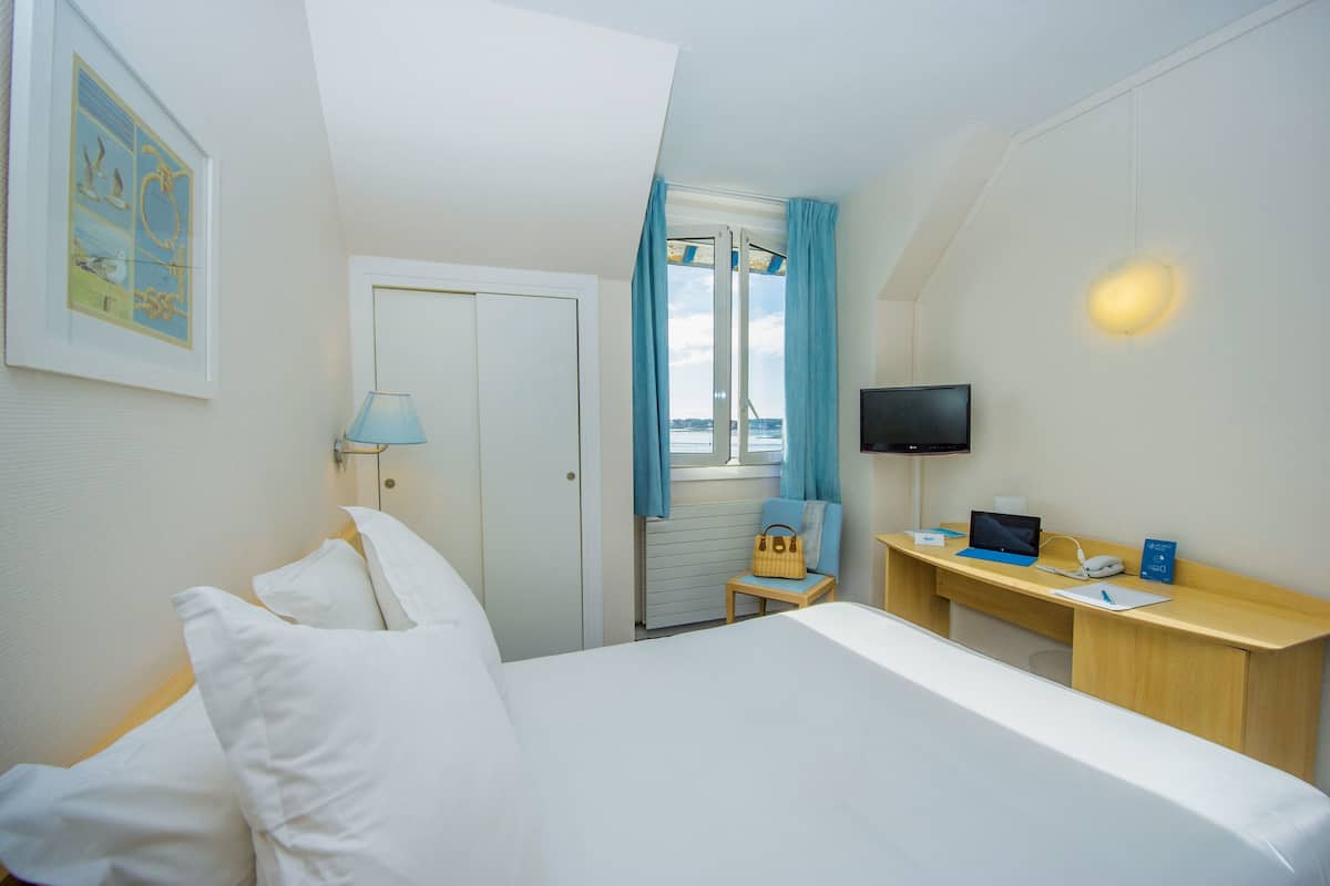 Une chambre d’hôtel avec un lit, un bureau avec un ordinateur portable, une télévision et une fenêtre avec des rideaux.