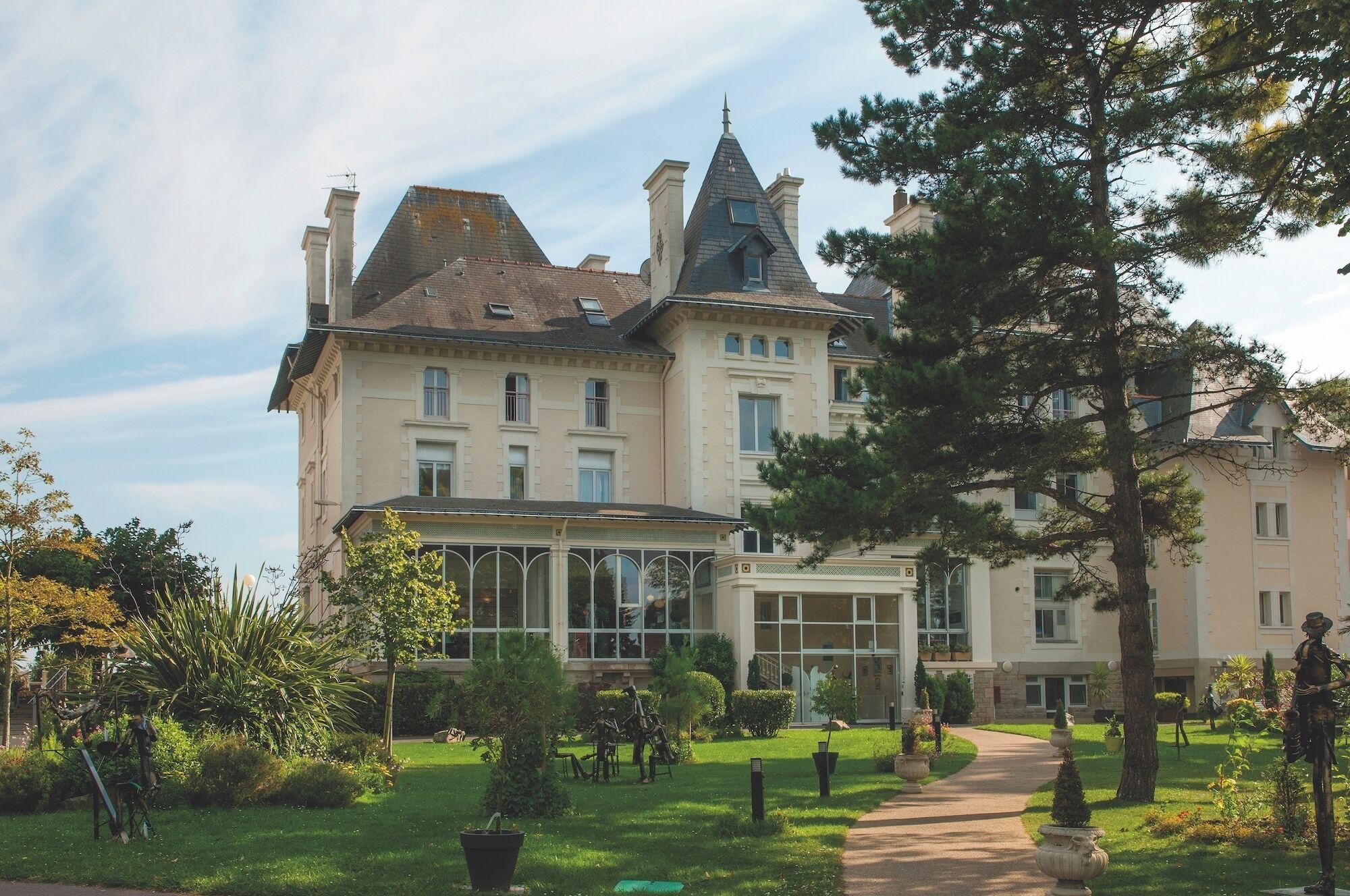 Un grand bâtiment historique à étages, doté d’une imposante verrière et d’un jardin bien entretenu agrémenté de sentiers.