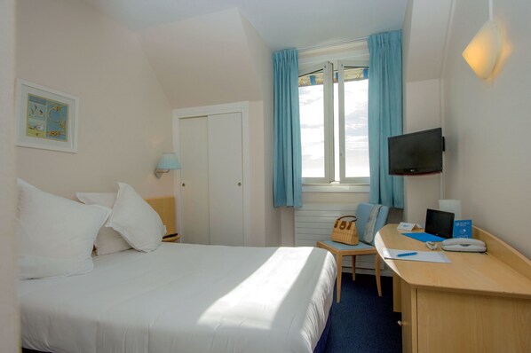 A hotel room with a bed, a desk with a computer, a television, and a window with curtains.