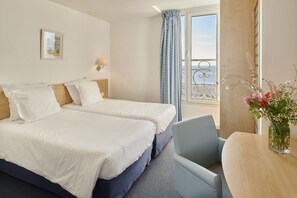 A hotel room with two beds, a desk, and a view of the sea. - Hôtel Vacances Bleues Villa Caroline (La Baule-Escoublac)