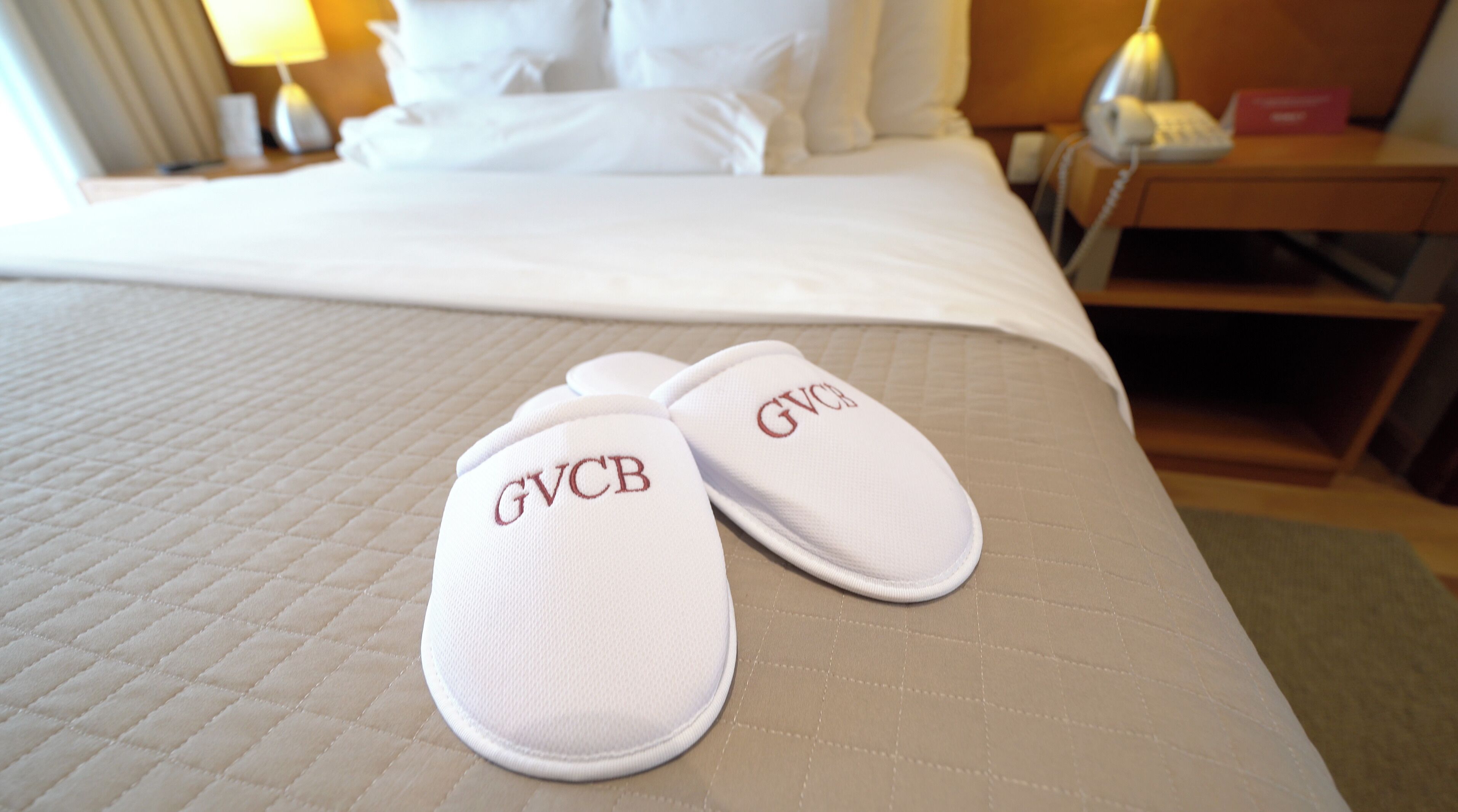 Una cama con una colcha acolchada y un par de pantuflas con texto bordado.