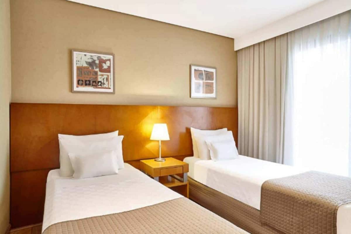 A hotel room with two beds, a nightstand with a lamp, and two framed pictures on the wall.