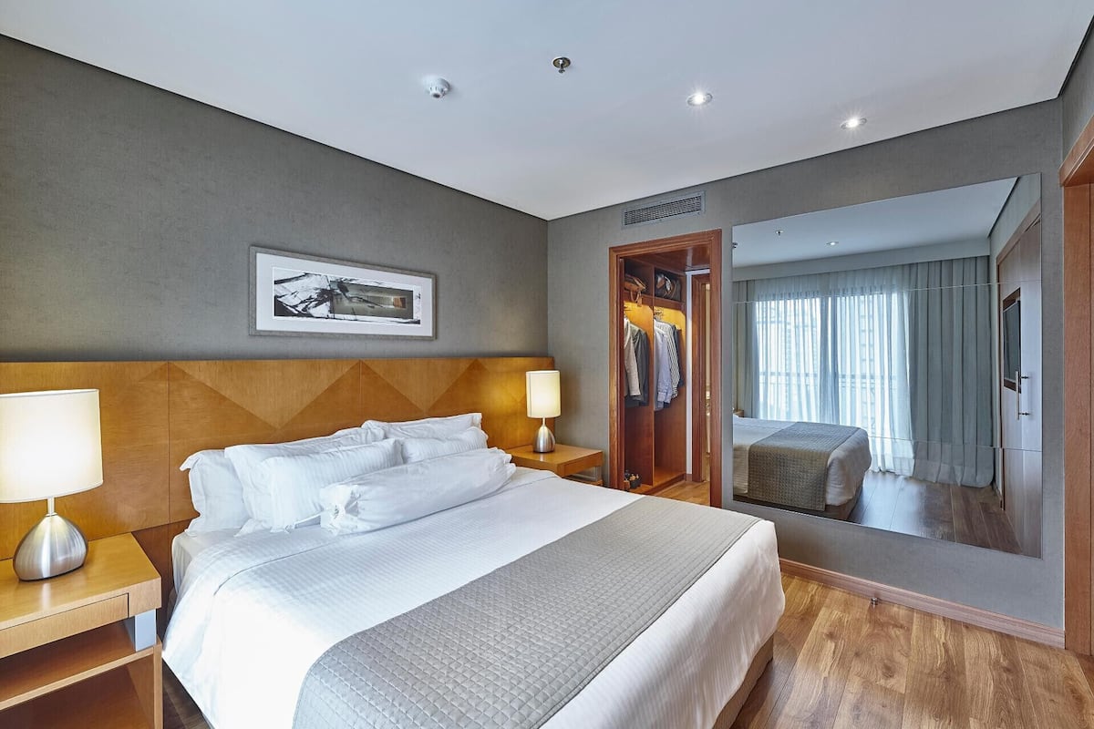 A hotel room with a large bed, a wooden headboard, a framed picture, a wardrobe, and a mirror.