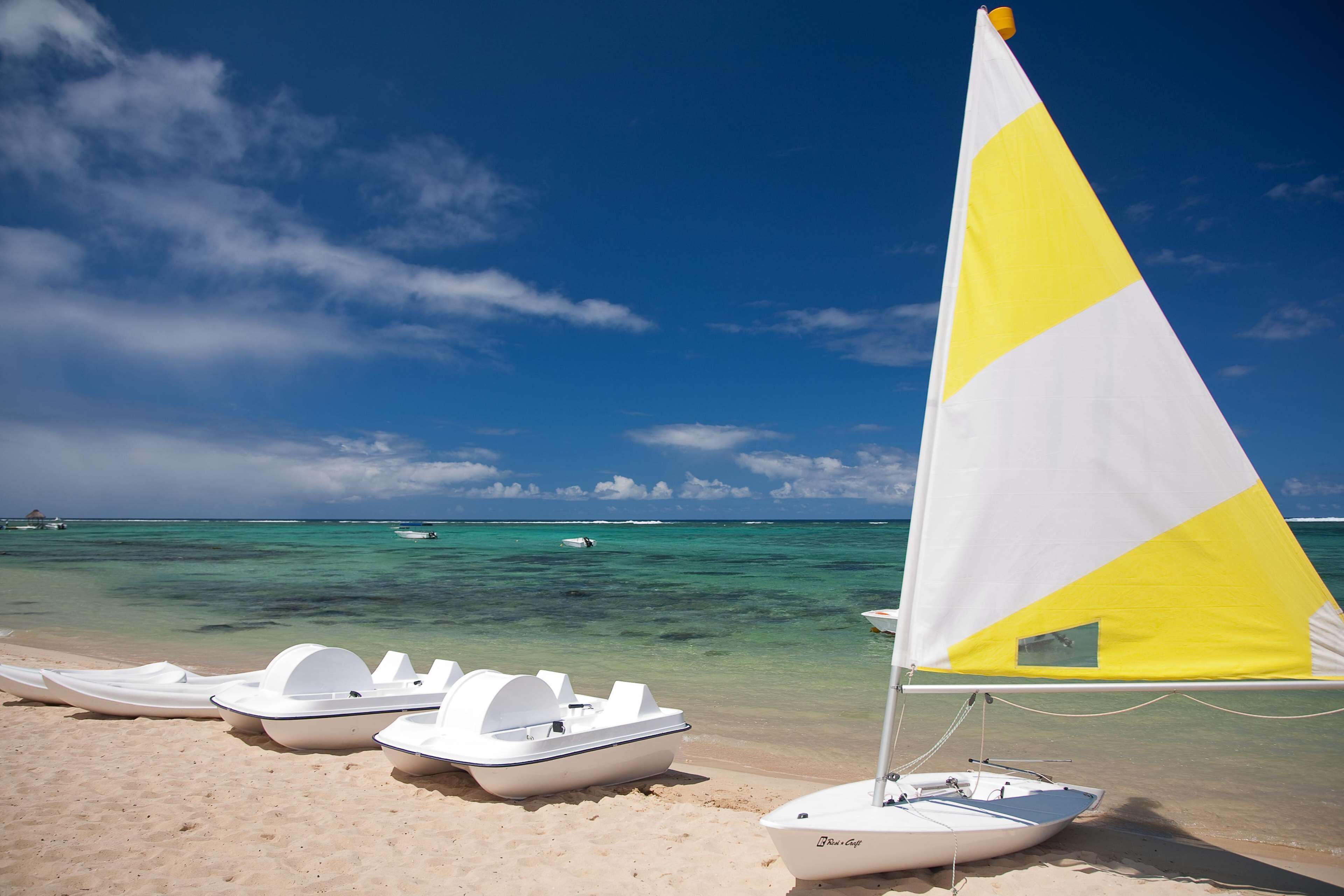 A beach with a sailboat and several small boats lined up on the sand.