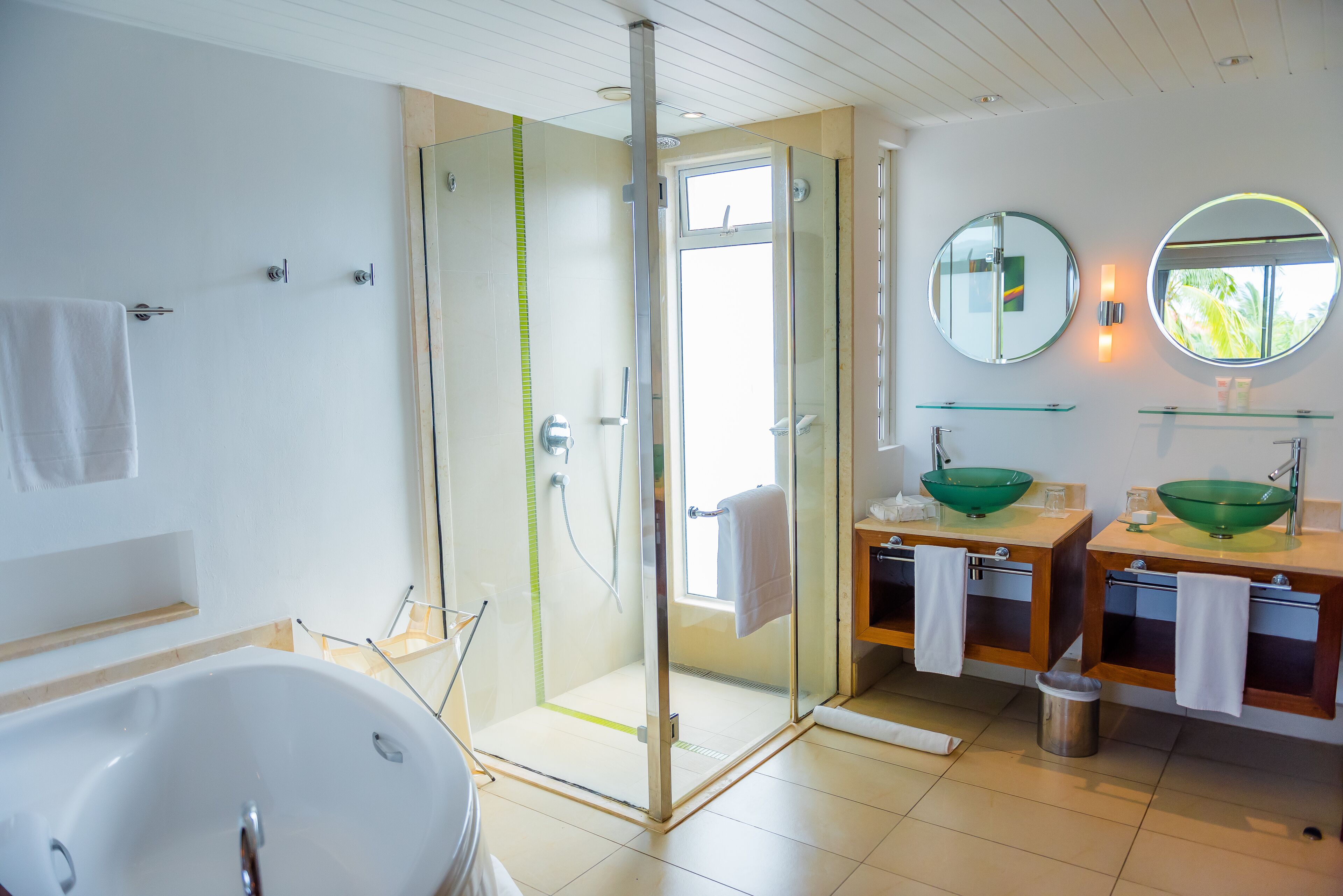 Une salle de bain moderne dotée d’une douche à parois de verre, d’une baignoire sur pieds et de deux vasques avec des cuves vertes.