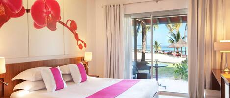 Habitación de hotel con una cama grande, vistas a la playa y un balcón con mobiliario exterior.