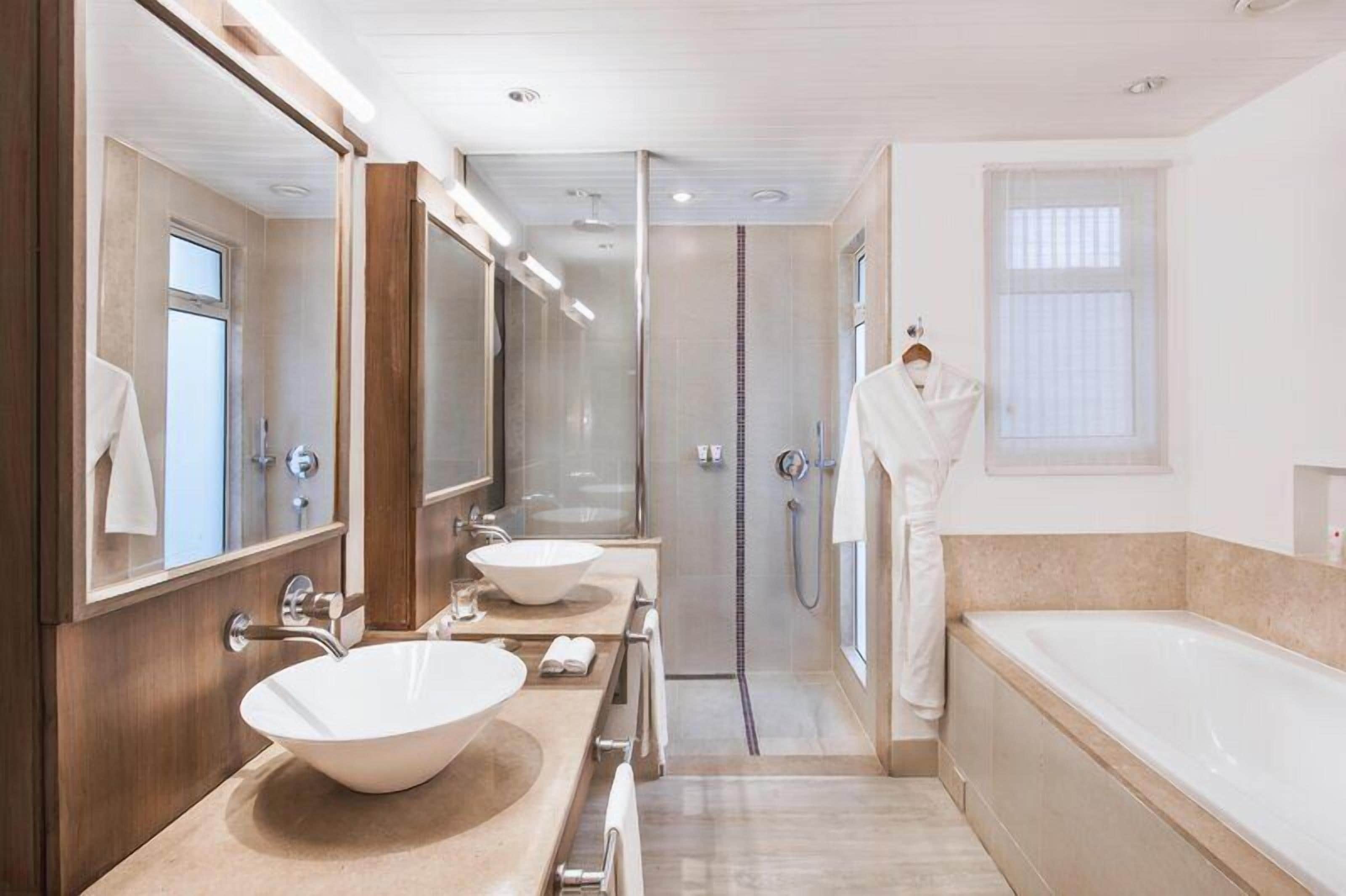 A modern bathroom with a large bathtub, two sinks, a walk-in shower, and a robe hanging on the wall.