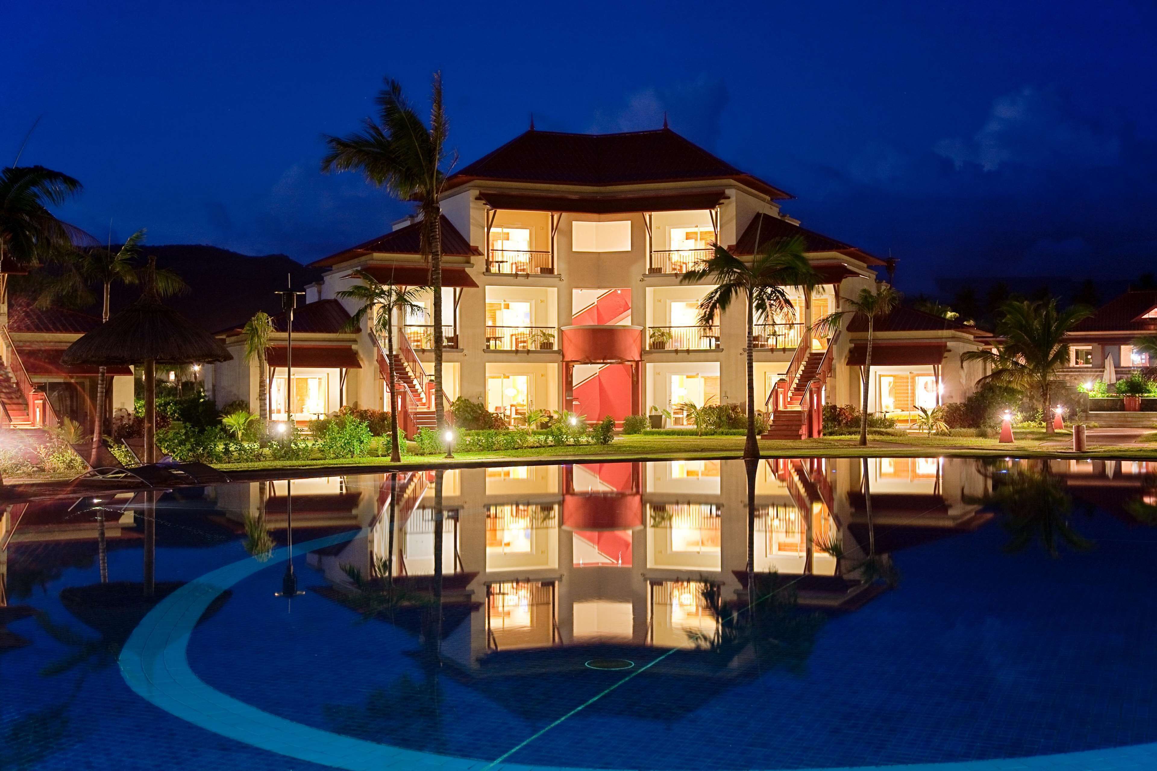 Un hotel de varios pisos con una escalera central, piscina y palmeras.