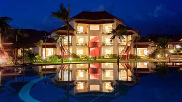 Un hotel de varios pisos con una escalera central, piscina y palmeras.