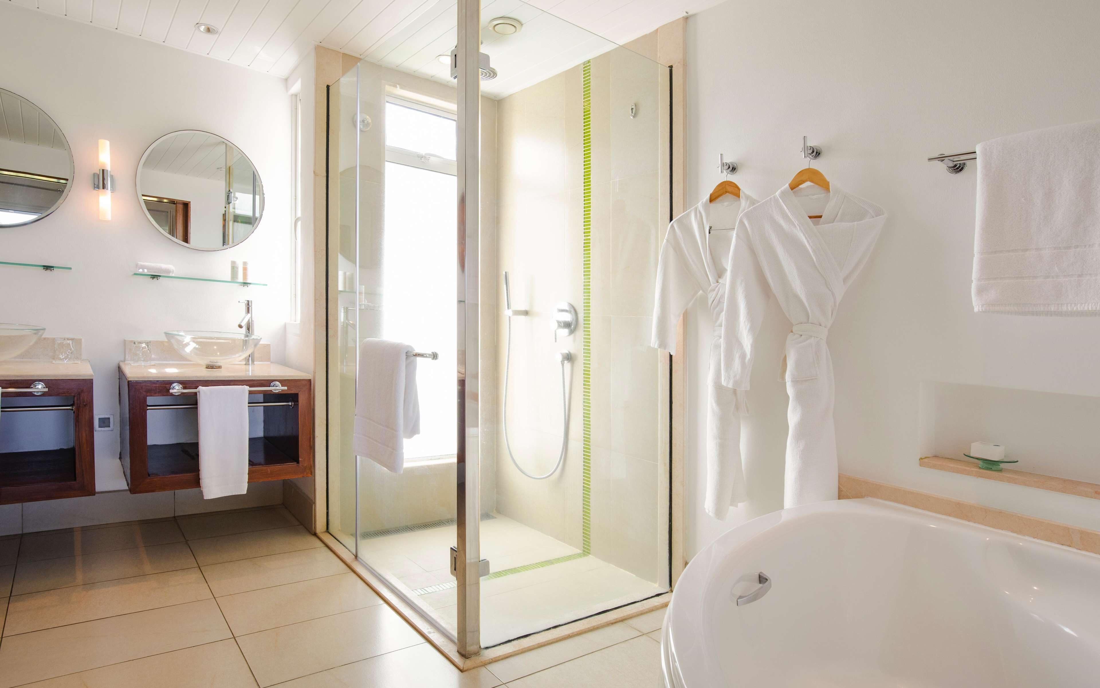 Un baño moderno con ducha de vidrio, una bañera y un tocador con dos lavamanos.