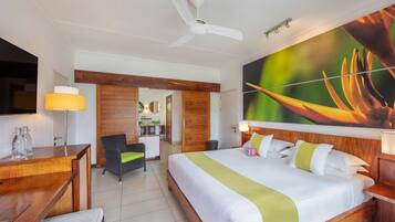 A hotel room with a bed, a desk, a chair, a ceiling fan, and a large wall painting.