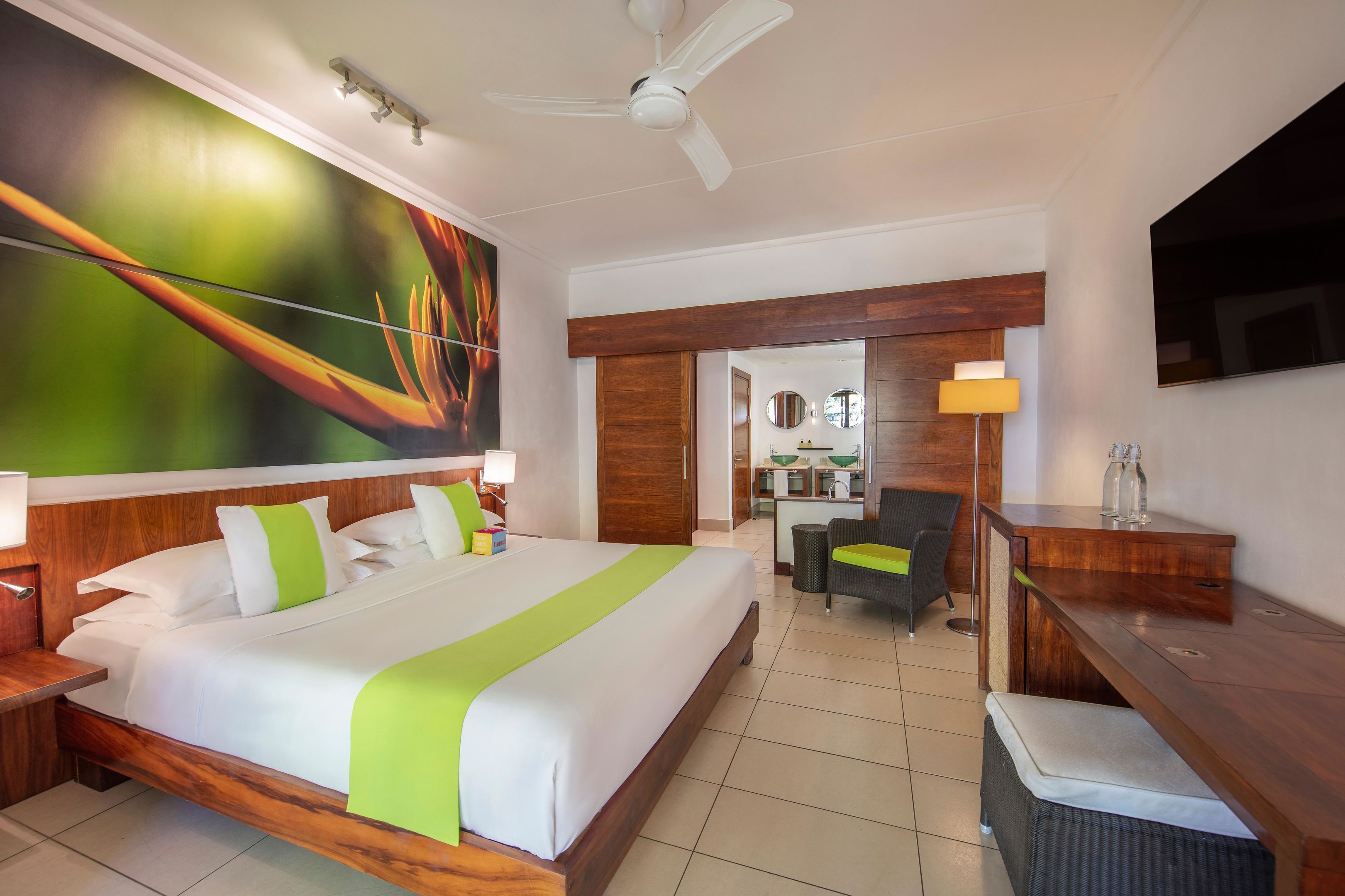 A hotel room with a large bed, a desk, a chair, a TV, and a ceiling fan.