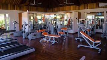 A gym with various exercise equipment, including treadmills and weight machines, under a wooden ceiling with natural light.