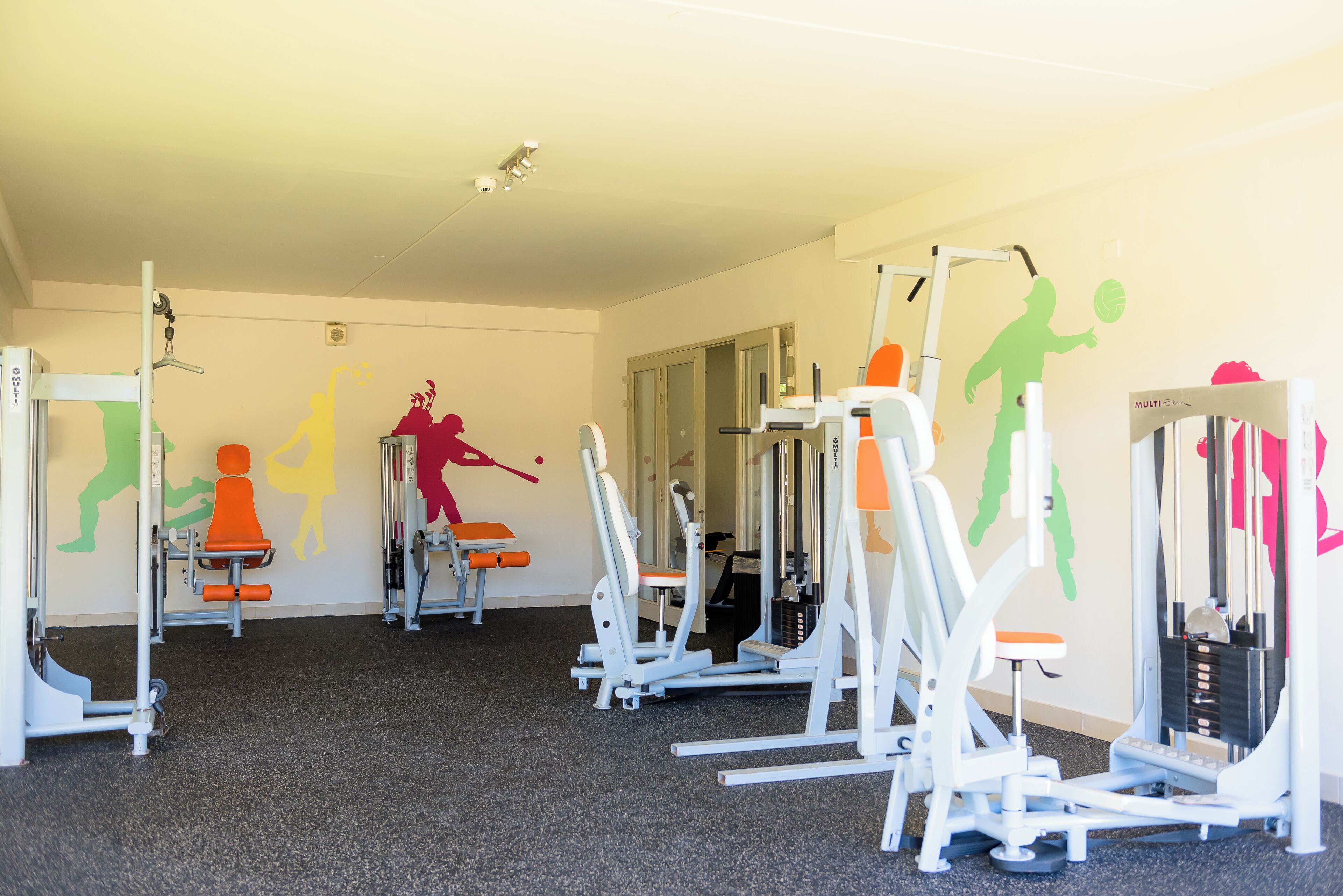 Un gimnasio con diversas máquinas de ejercicio y coloridos murales en las paredes.