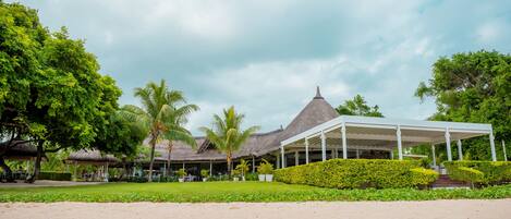 A resort with a covered outdoor area, palm trees, and a thatched-roof building.