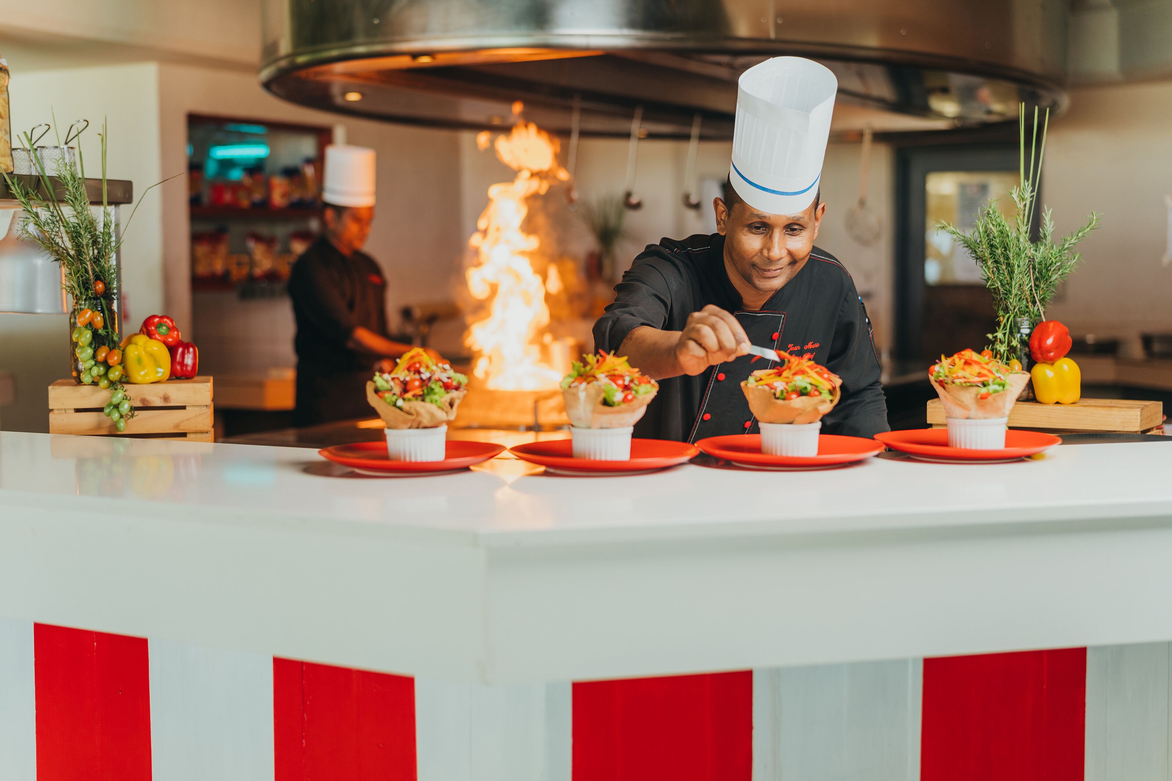 Un chef preparando platos en una barra con una cocina moderna al fondo.