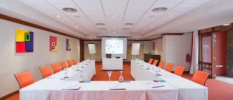 A conference room with a long table, orange chairs, and a projector screen.
