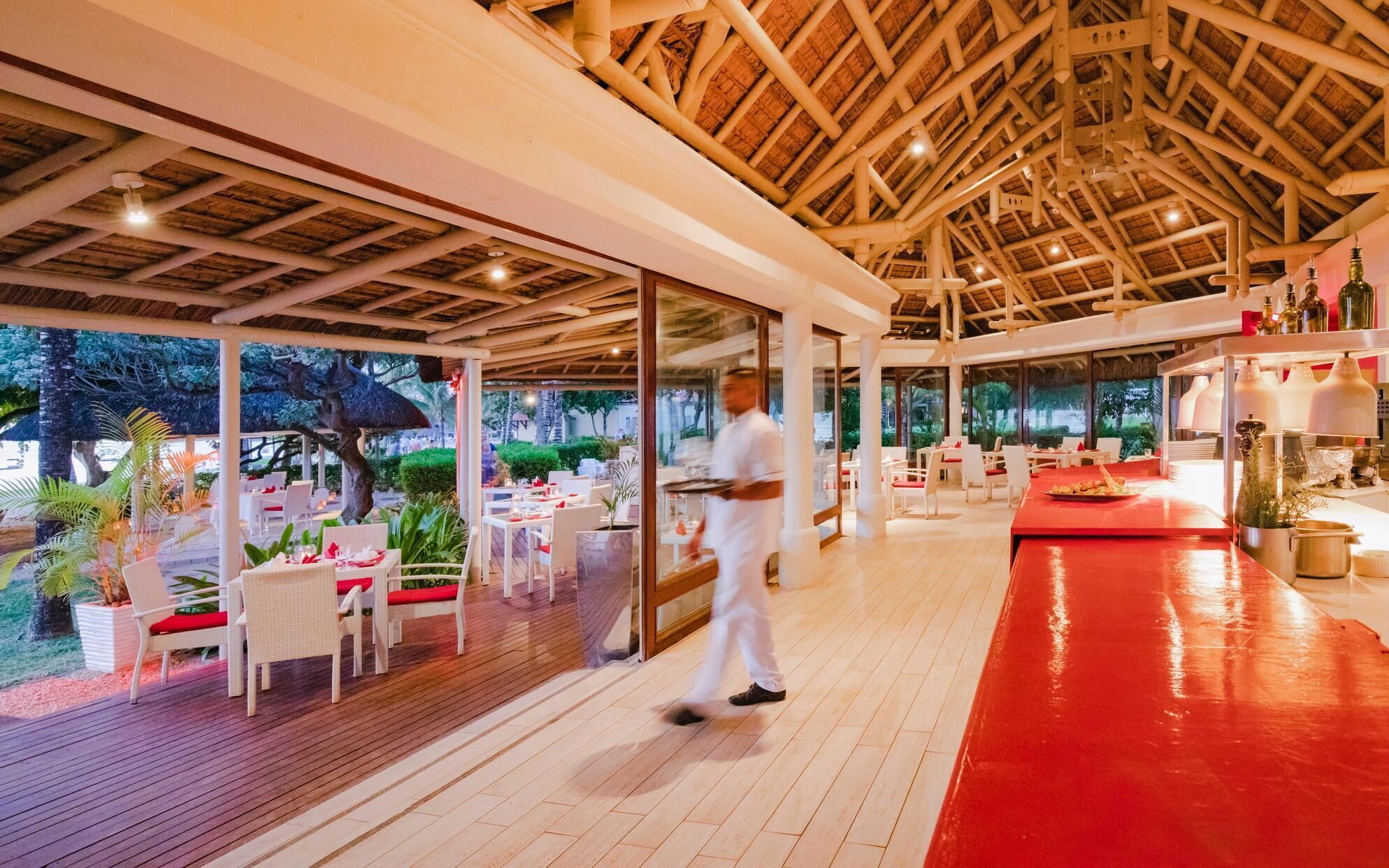 Un comedor interior con techo de madera, mesas con sillas blancas y alfombra roja.