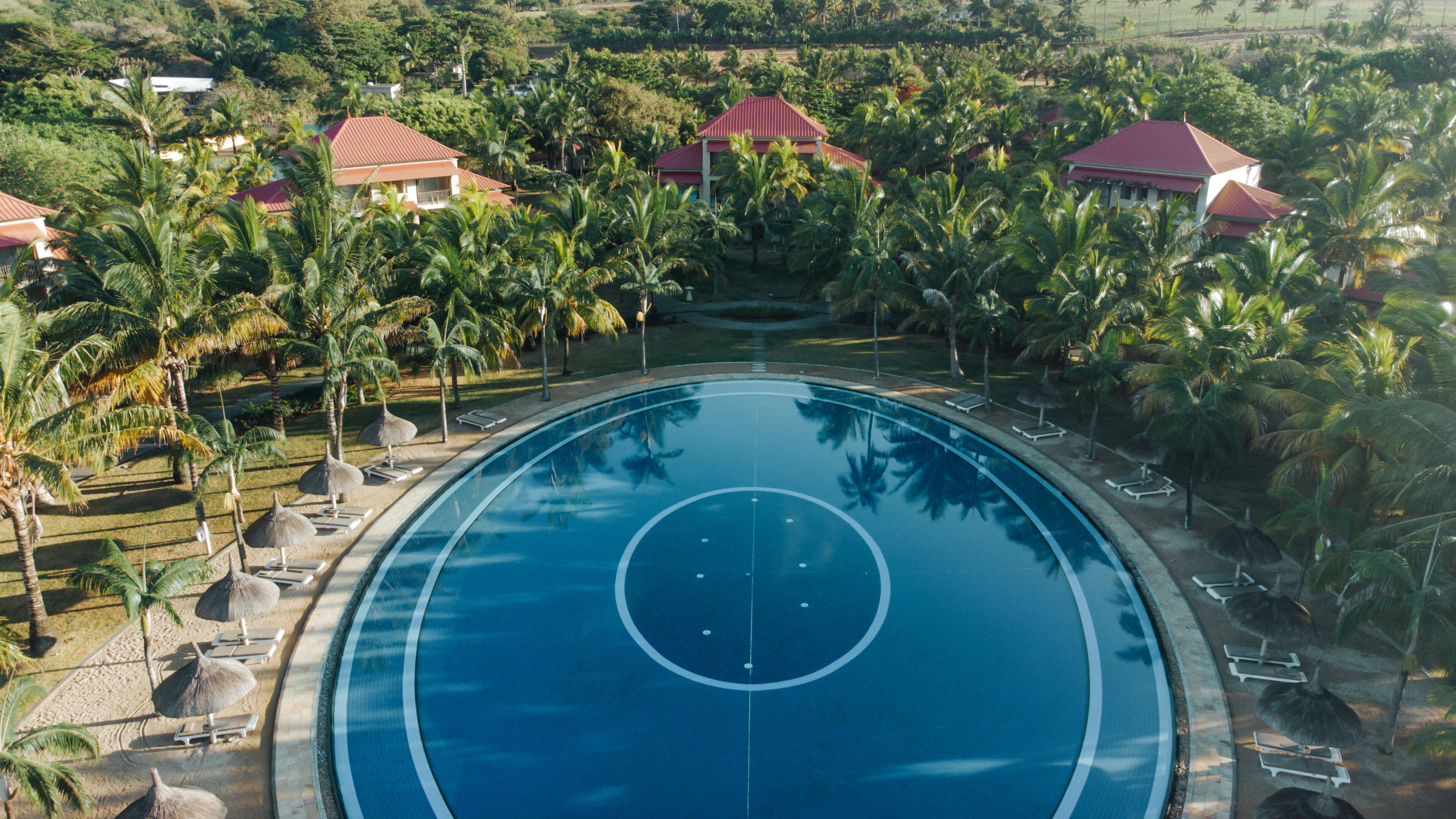 Una vista aerea di un resort con una grande piscina circondata da palme e lettini.