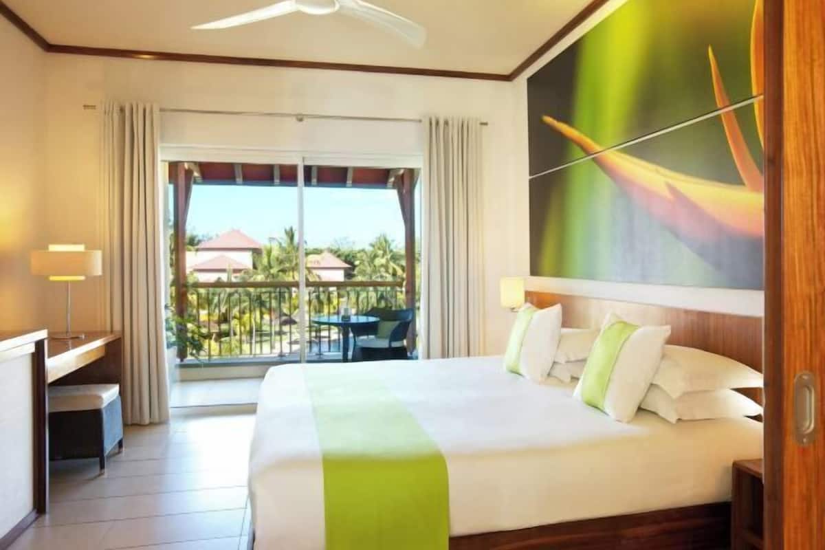 Une chambre d’hôtel avec un grand lit, un bureau, une chaise, un balcon avec vue et un ventilateur de plafond.