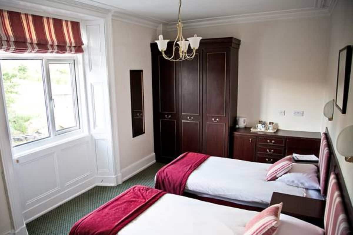 Habitación de hotel con dos camas, un armario, una araña y un ventanal con cortinas.
