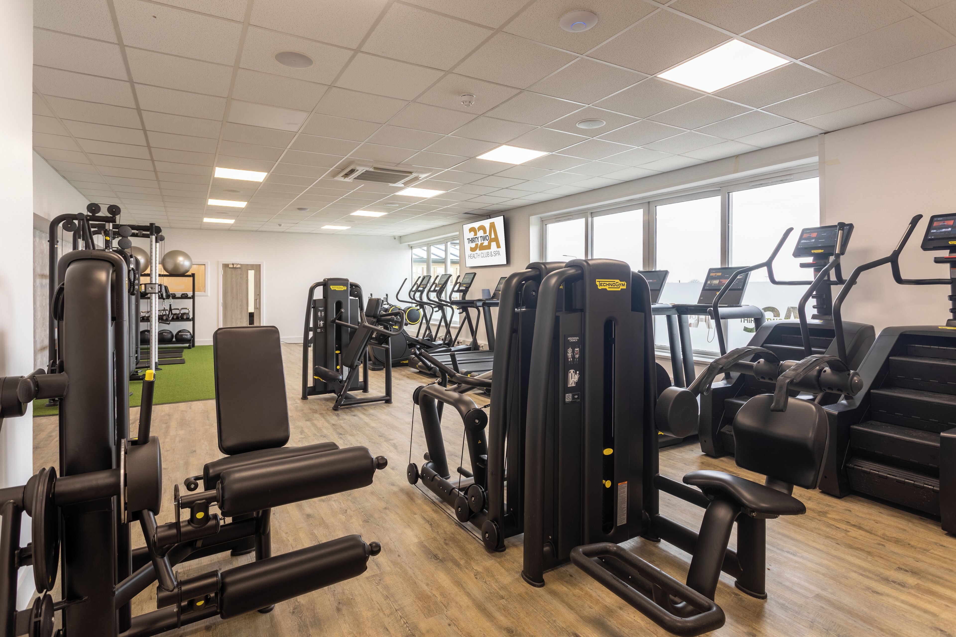 Un gimnasio con diversos equipos de ejercicio, un ventanal grande y un cartel que indica membresía por 30 días.