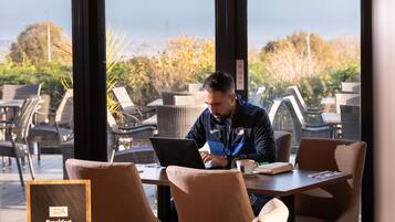 A man working on a laptop at a table with a view of outdoor seating and greenery.