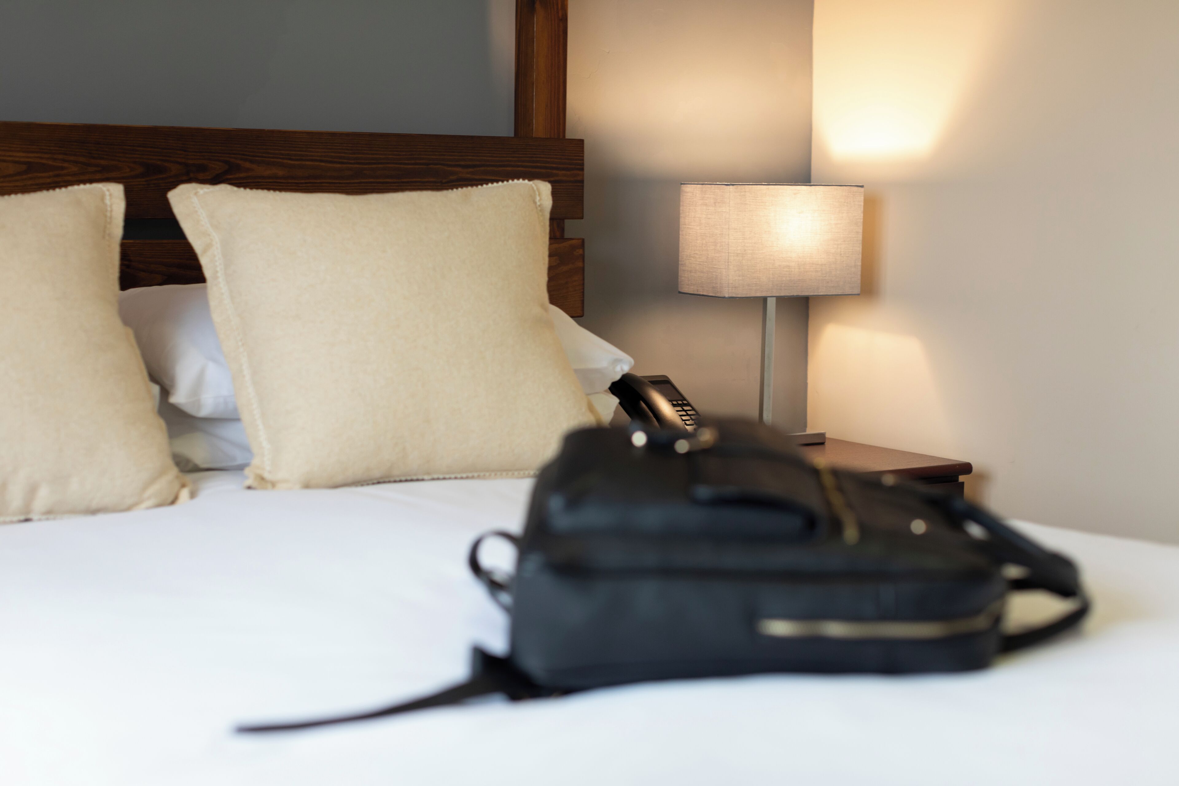 Un lit avec des oreillers, une lampe de chevet et un sac noir posé sur le lit.